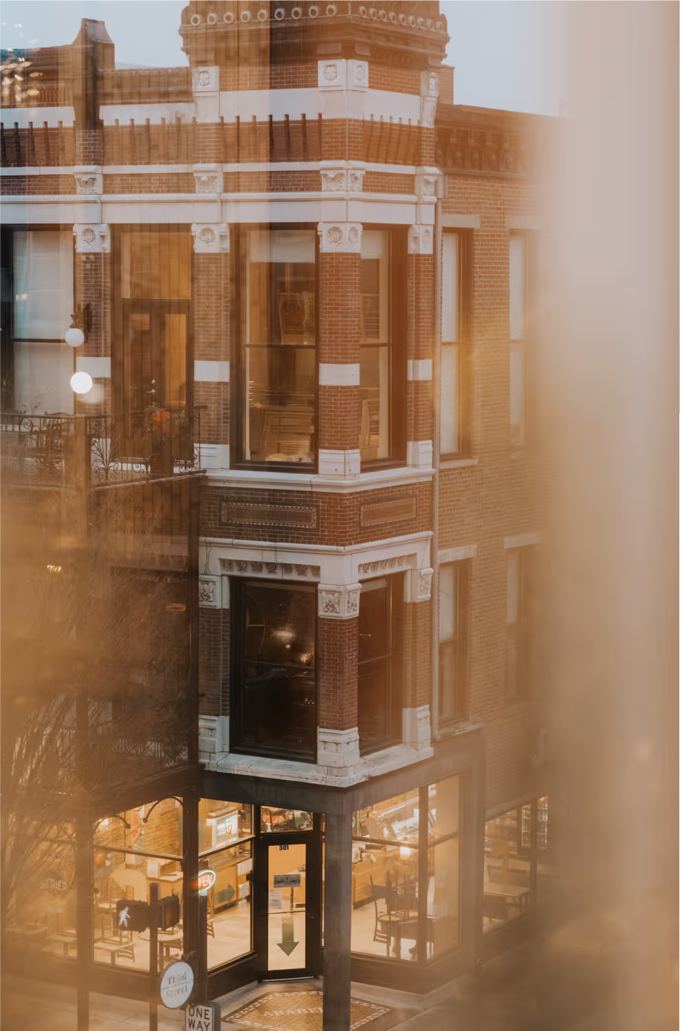 A beautiful brick building corner featuring a Christmas tree inside, illuminated windows, and street signage in a cozy urban setting.