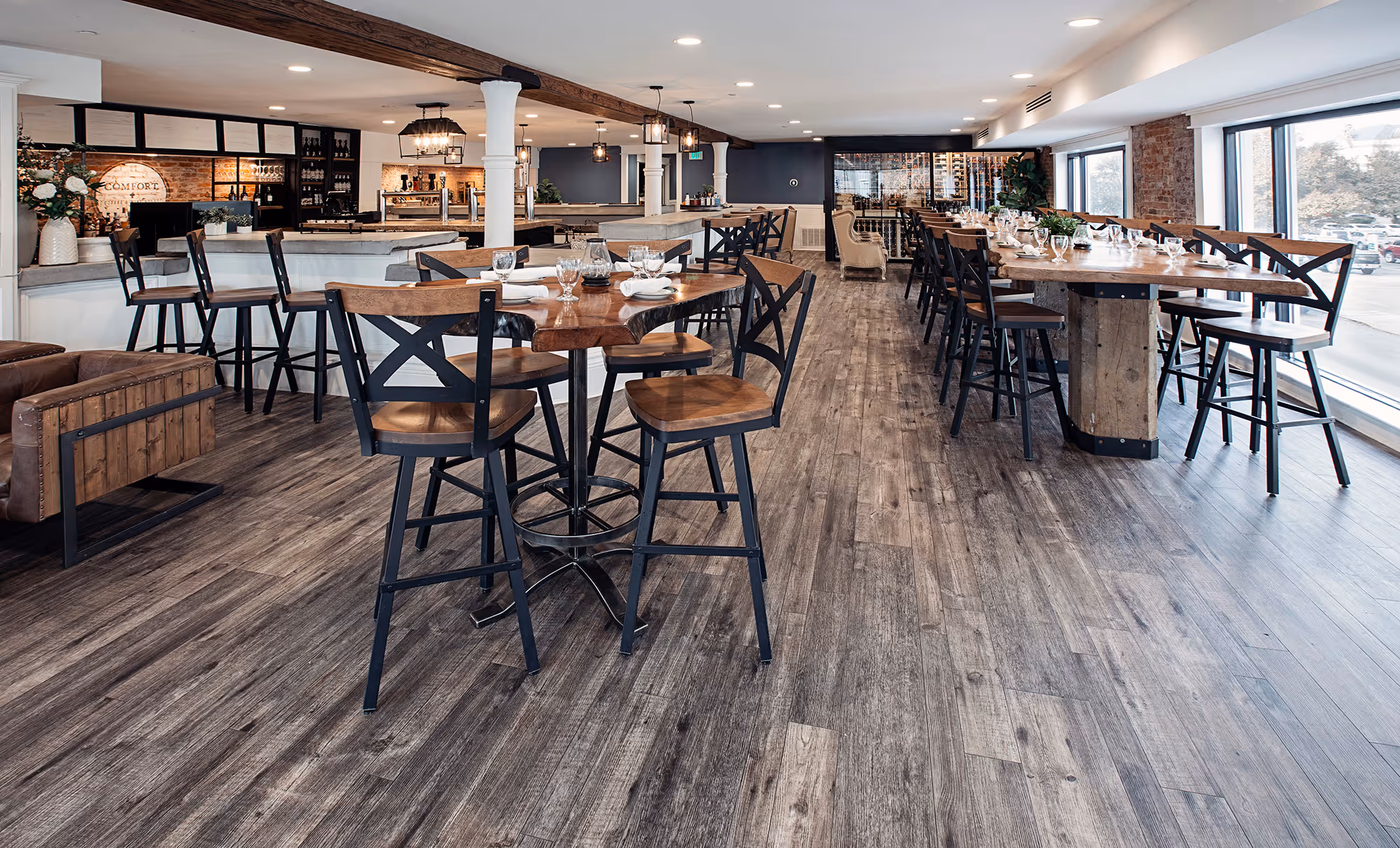 Stylish restaurant interior with wooden floors, high-top tables, and a welcoming bar area, featuring warm lighting and modern decor.