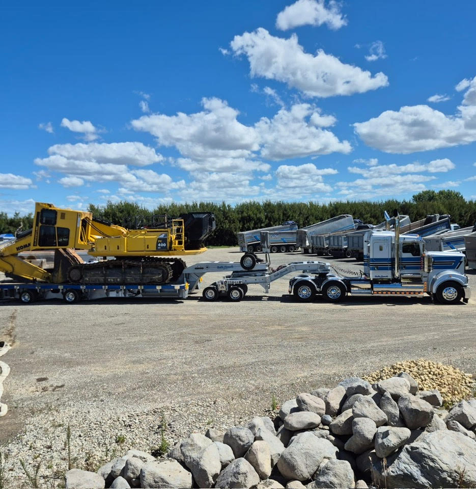 AC98 Heavy Haulage team using a mobile crane to lift and load large steel machinery components onto a Kenworth transporter for delivery across New Zealand.