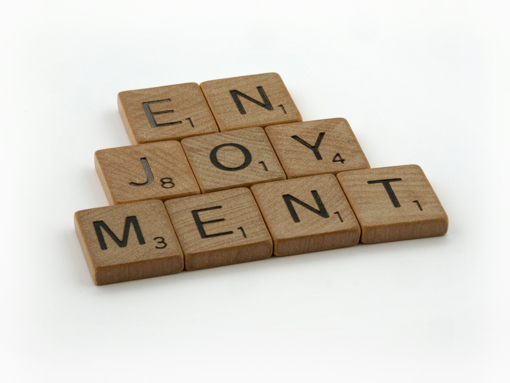 Wooden letter tiles arranged to spell “enjoyment” on a light background.