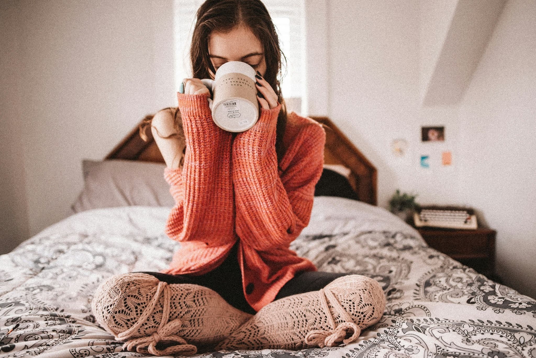 Person enjoying a peaceful morning routine on a bed with a beverage in a mug.