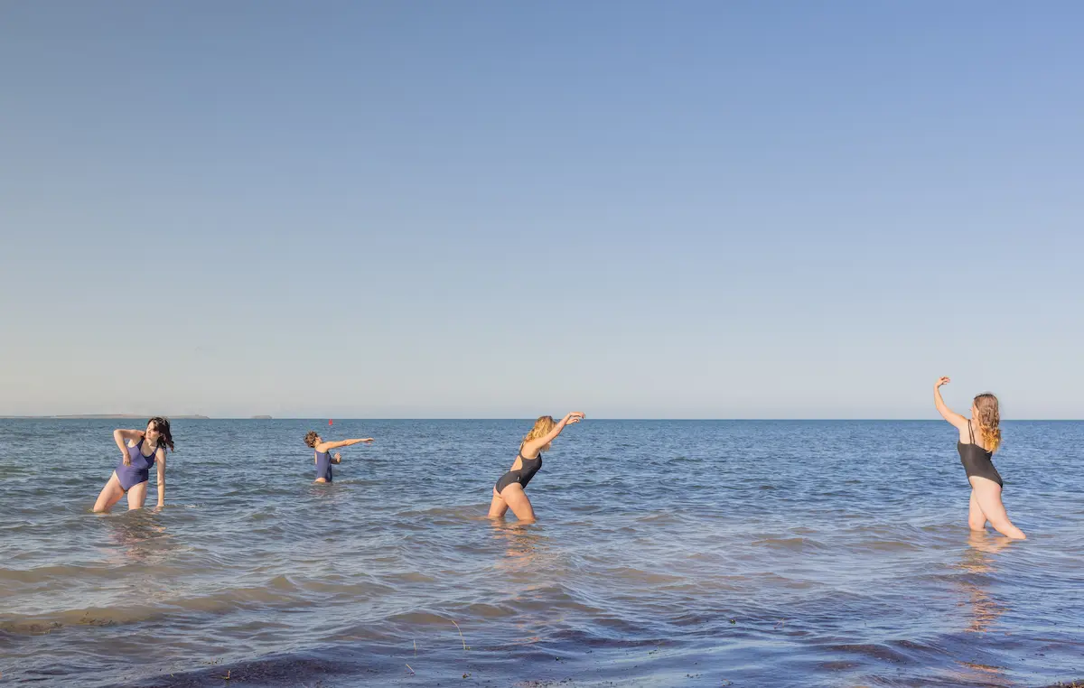 Image credit: Noa Smith-Fletcher. Three figures moving in knee-deep seawater, the sky and sea are blue.