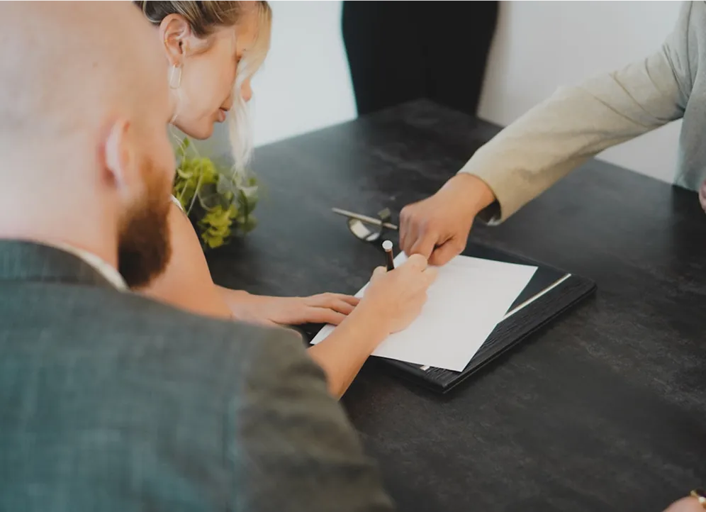 People signing document at desk with white paper and pen
