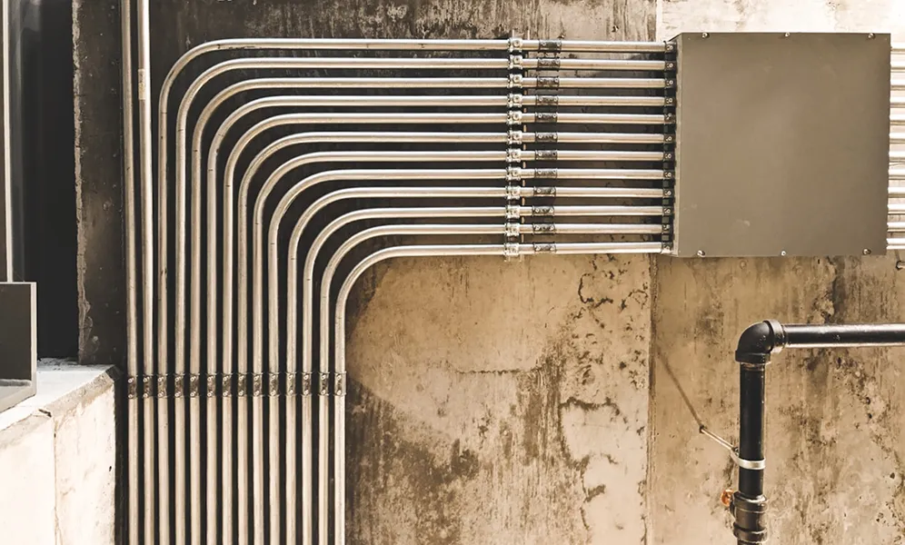 Curved metal pipes and conduits mounted on aged concrete wall
