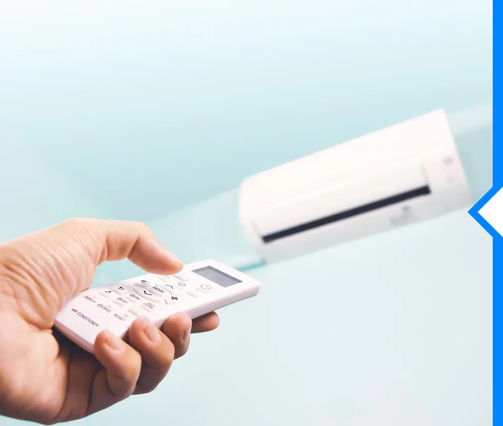 Hand holding remote control pointed at white wall-mounted air conditioner