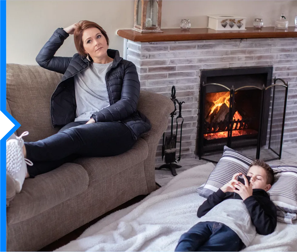 Person looking stressed on couch near fireplace while child uses device