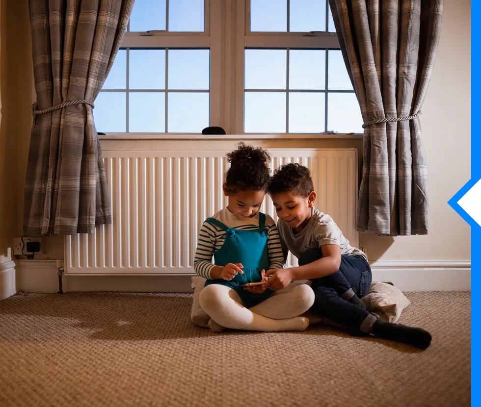 Two children sitting together by window, looking at something on floor