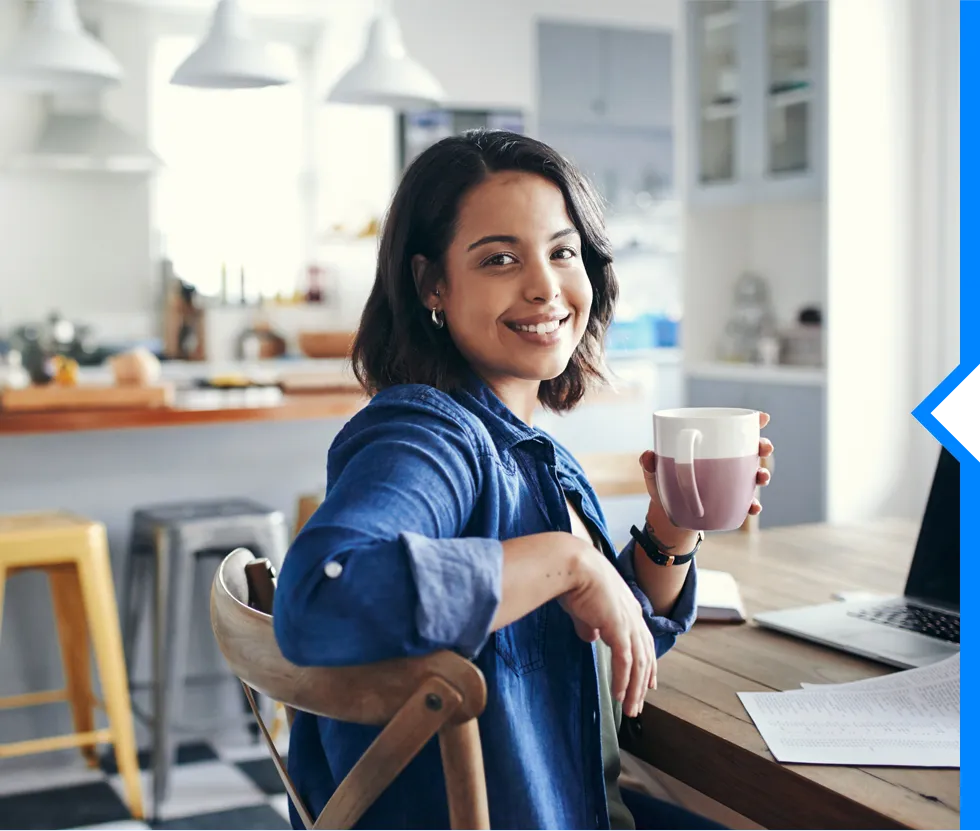 Smiling woman in blue shirt holding coffee mug at home workspace