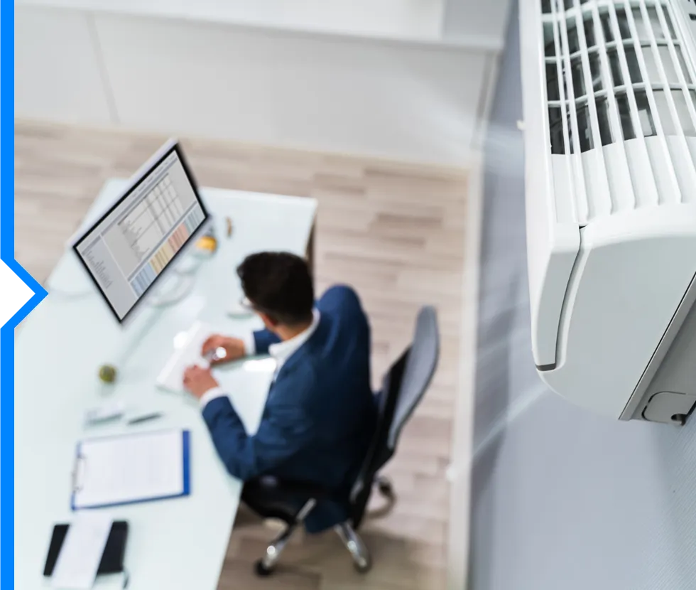 Person working at desk with computer, clipboard, and air conditioning unit