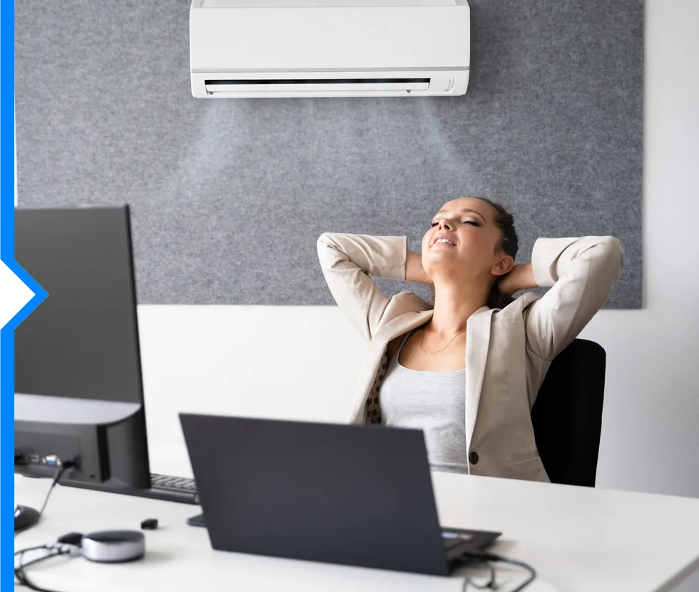 Person relaxing at desk with air conditioner, leaning back with eyes closed