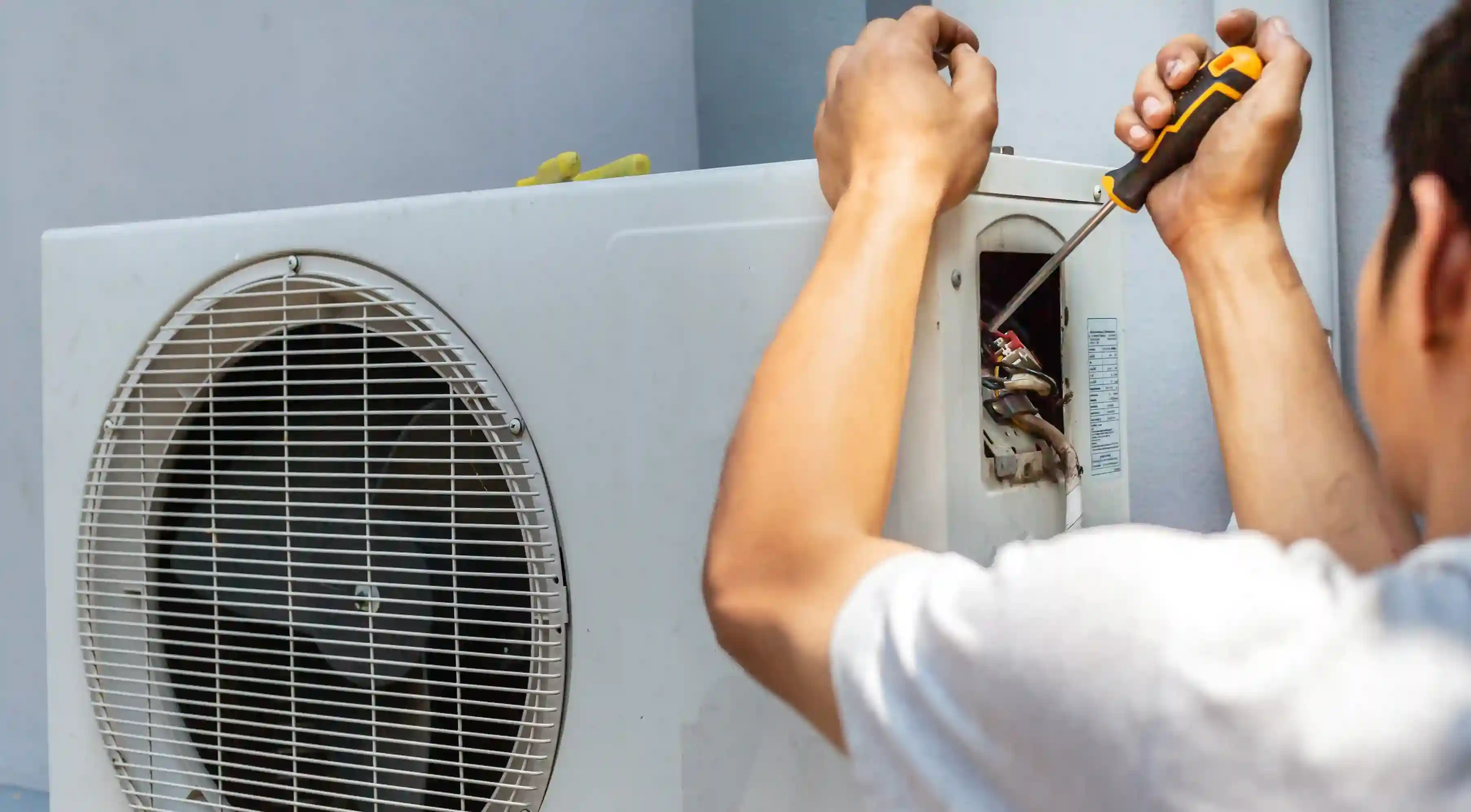 Technician in white shirt servicing outdoor AC unit with open panel and visible fan grille