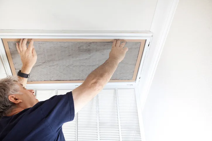 Person installing air filter into ceiling-mounted HVAC vent using both hands