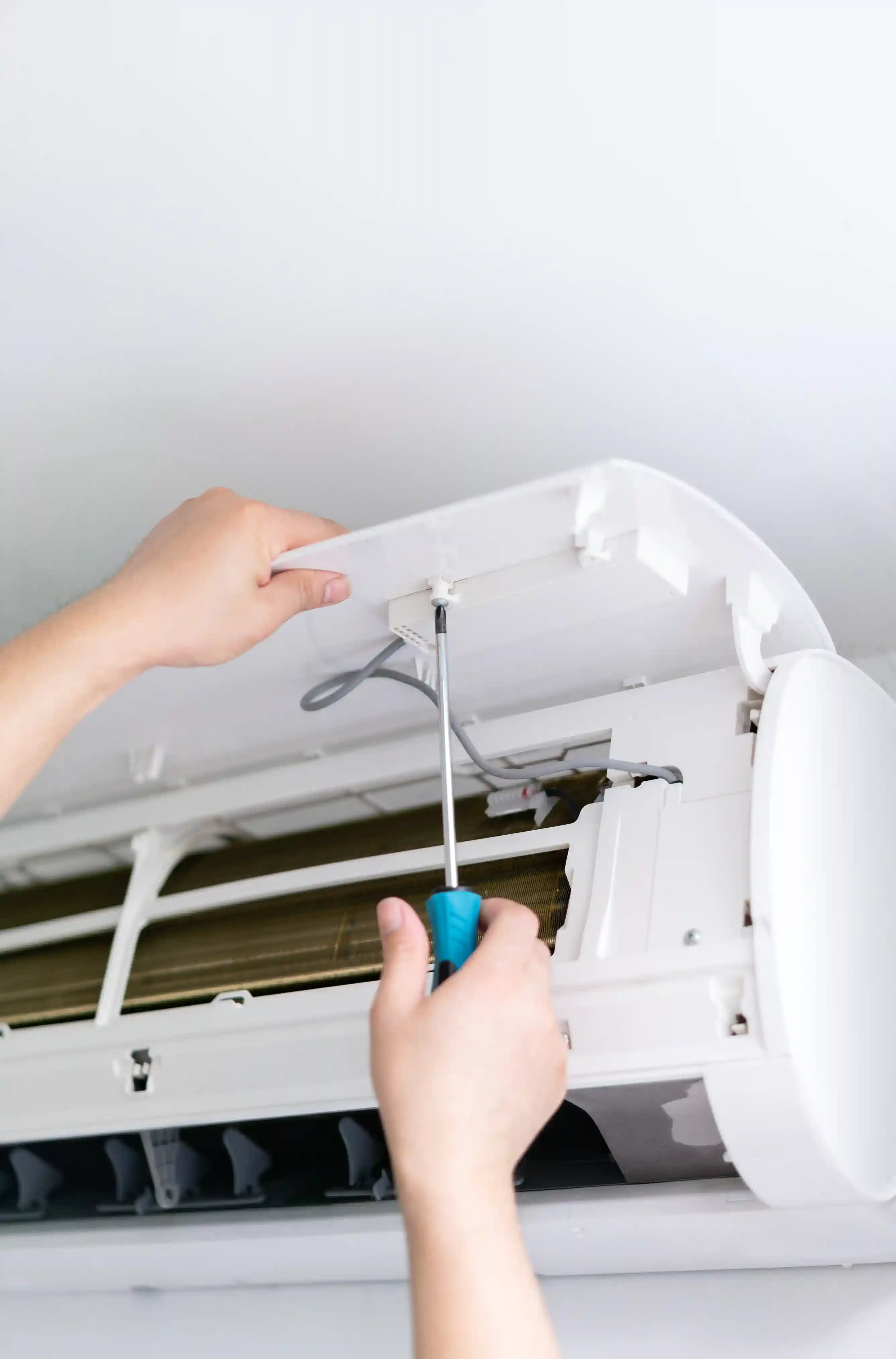 Hands using screwdriver to repair or maintain a white air conditioning unit