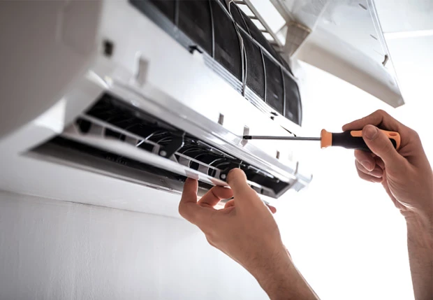 Technician repairing air conditioning unit with screwdriver