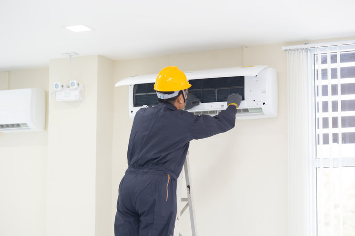 Technician in yellow hard hat repairing air conditioning unit on wall