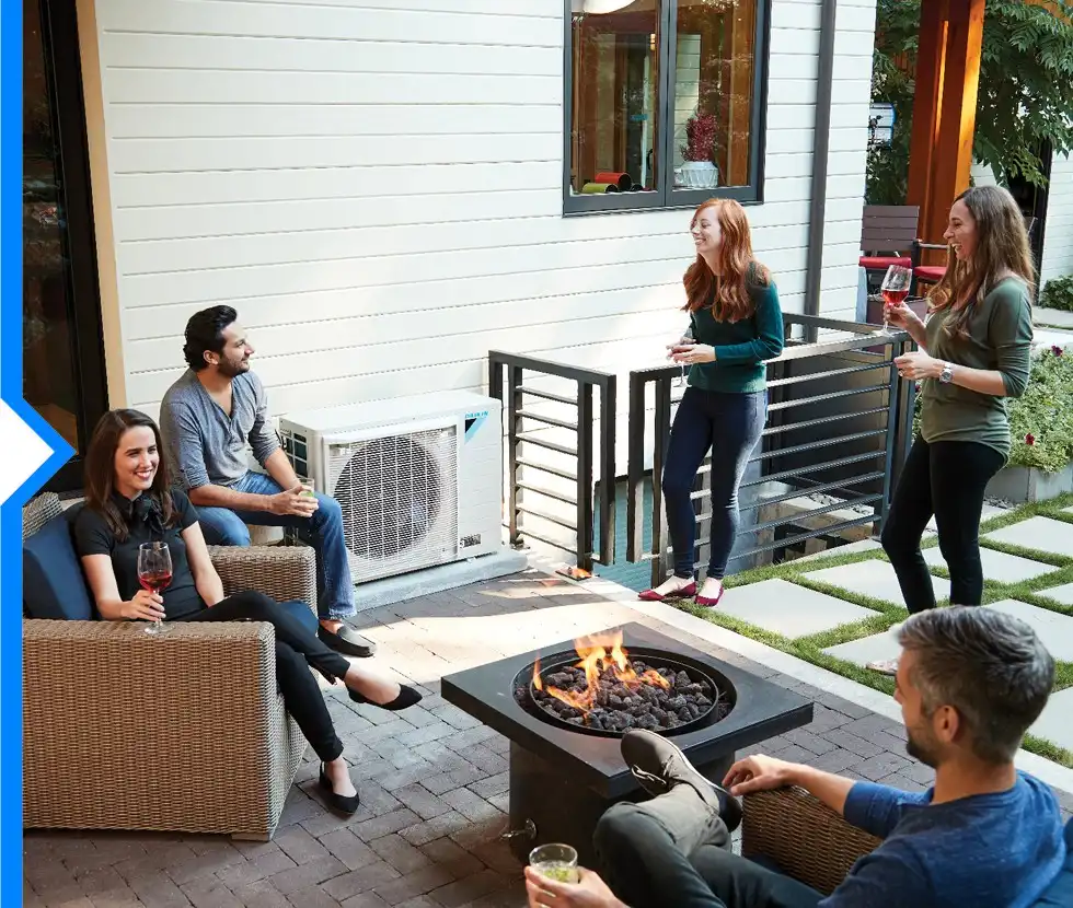A group of five friends is socializing on a patio with a fire pit, with a Daikin FIT air conditioning unit visible next to the house.