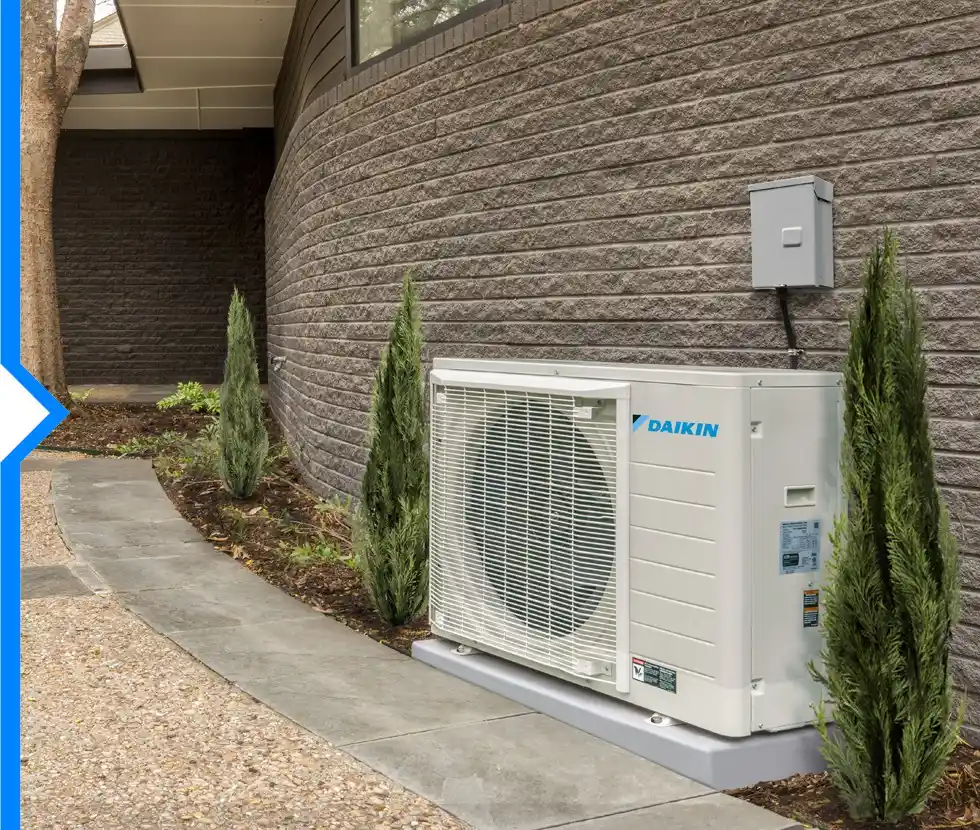 A white Daikin FIT air conditioning unit is installed on a gray pad next to a curved walkway and a stone wall.