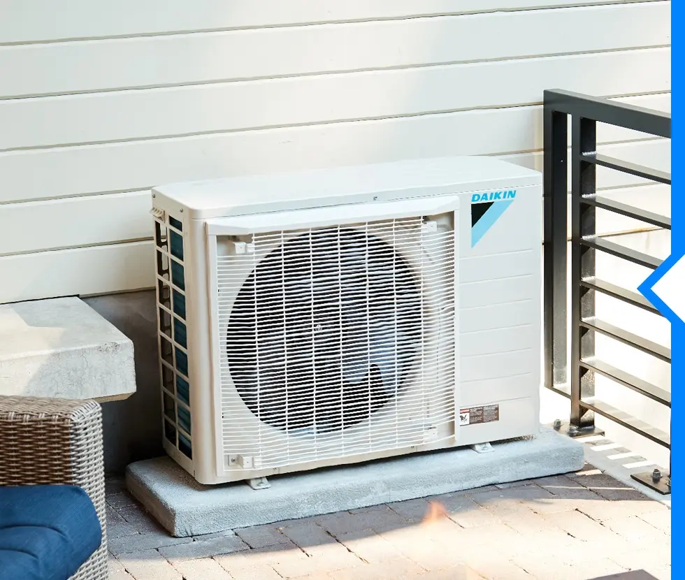 A Daikin FIT air conditioning unit is installed on a gray block next to a patio with wicker furniture and a railing.