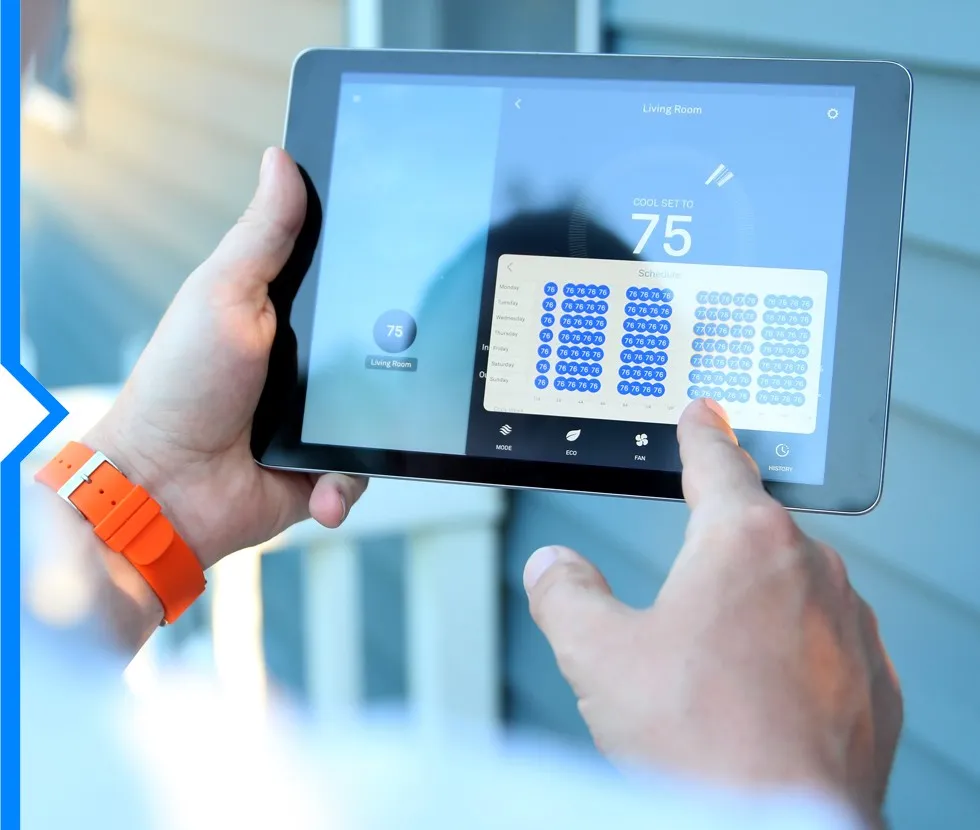 A person is holding a tablet that displays an HVAC control app with temperature settings and a weekly schedule.
