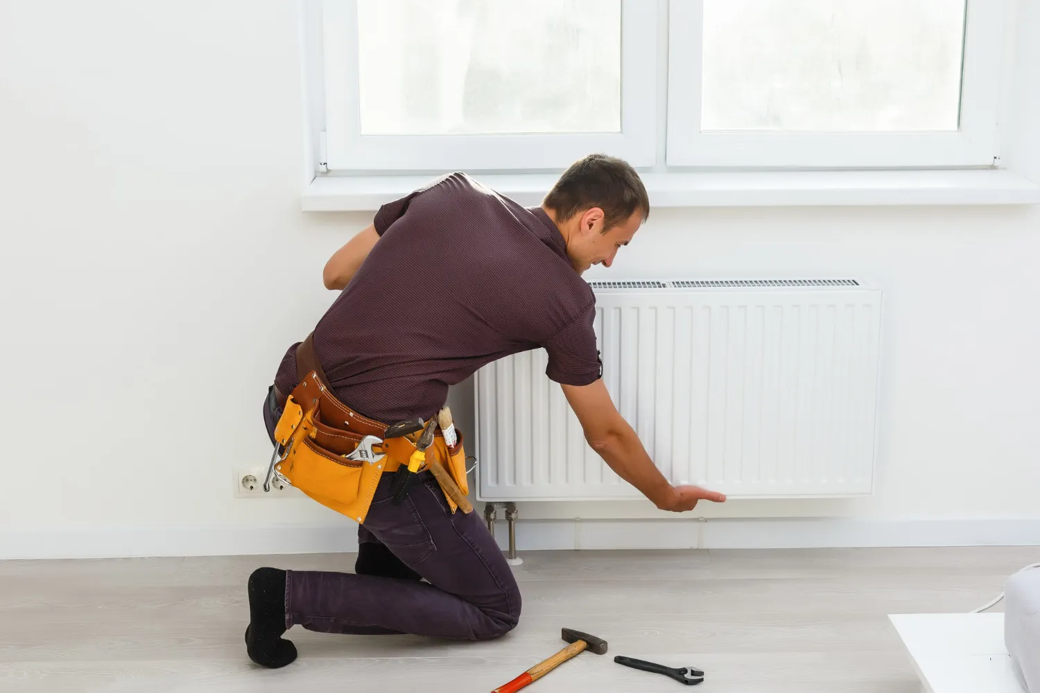 Plumber working on radiator with tools, wearing yellow tool belt