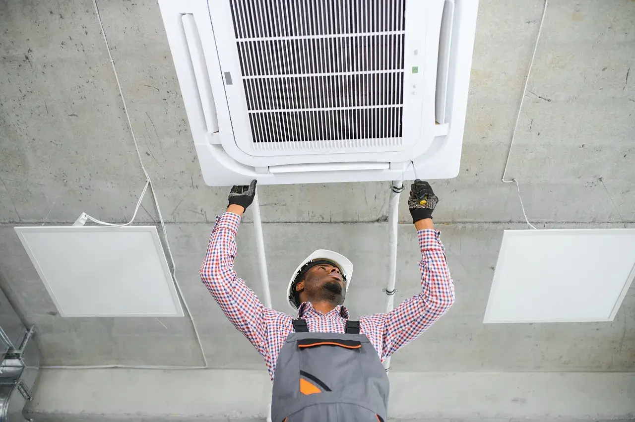 Technician installing ceiling-mounted air conditioning unit with safety gear