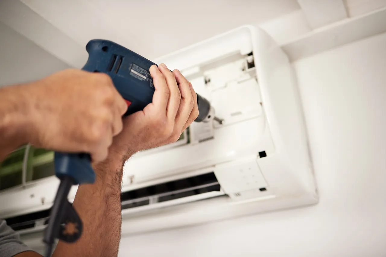 Technician installing or repairing air conditioning unit with power drill