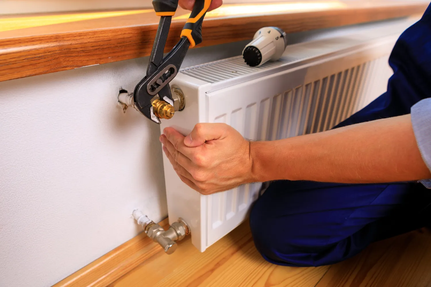 Plumber using pliers to repair a radiator valve on a white heater