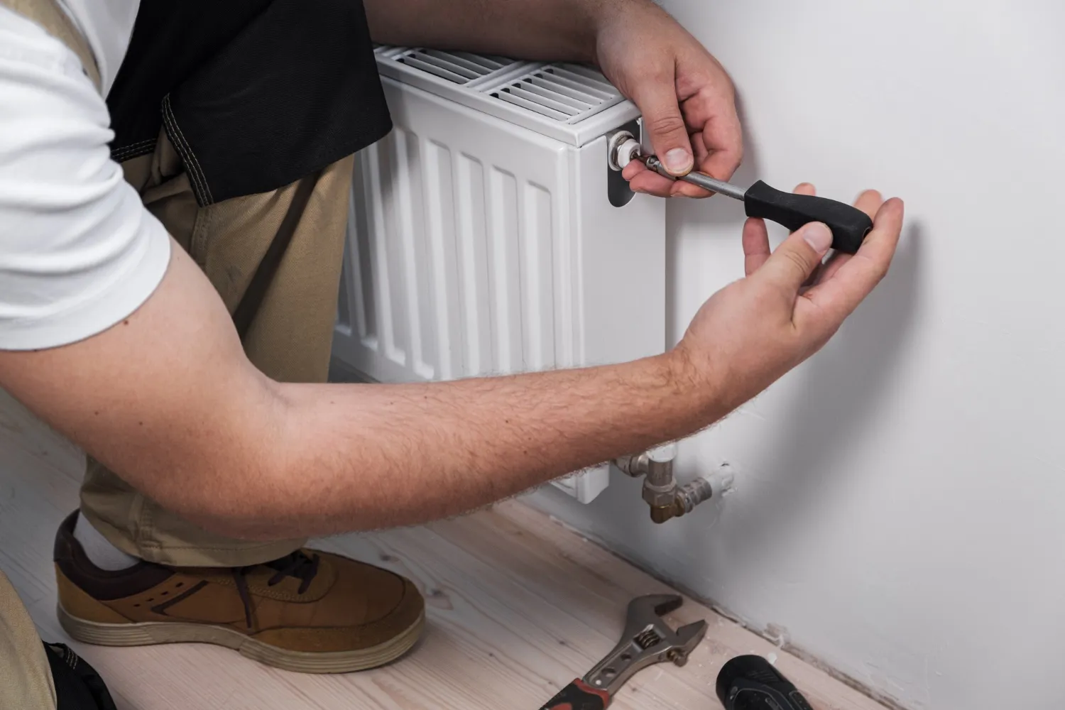 Plumber adjusting radiator valve with wrench on white wall