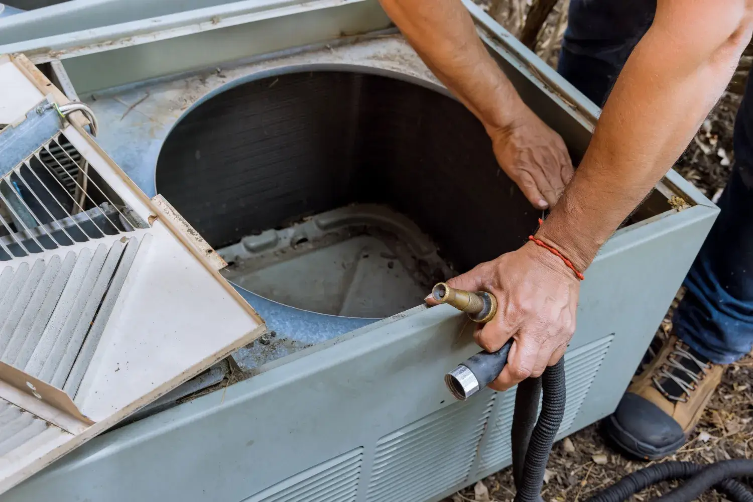 Technician servicing an air conditioning unit with a water hose