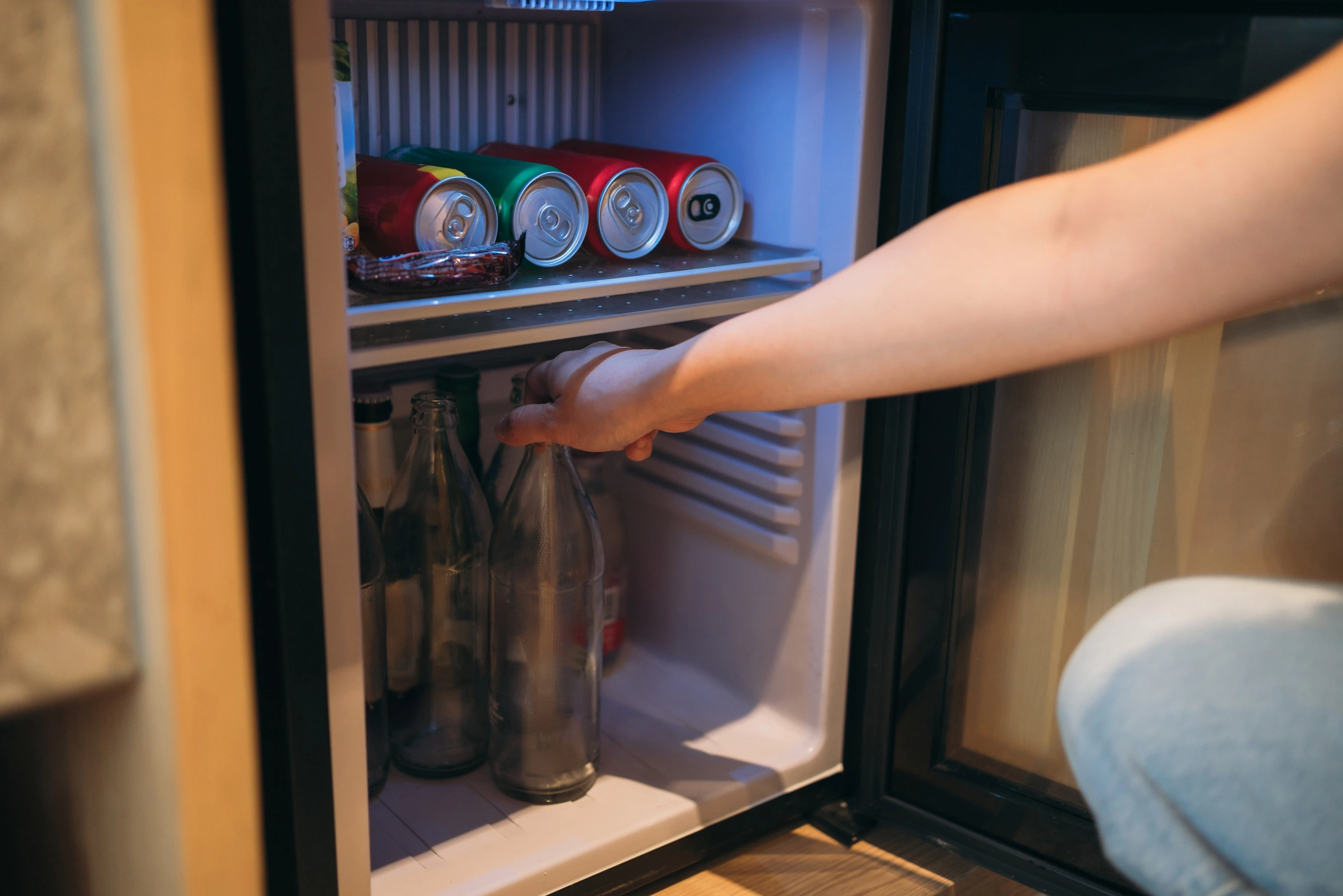 A person opens a small refrigerator, preparing for beverage cooler installation.