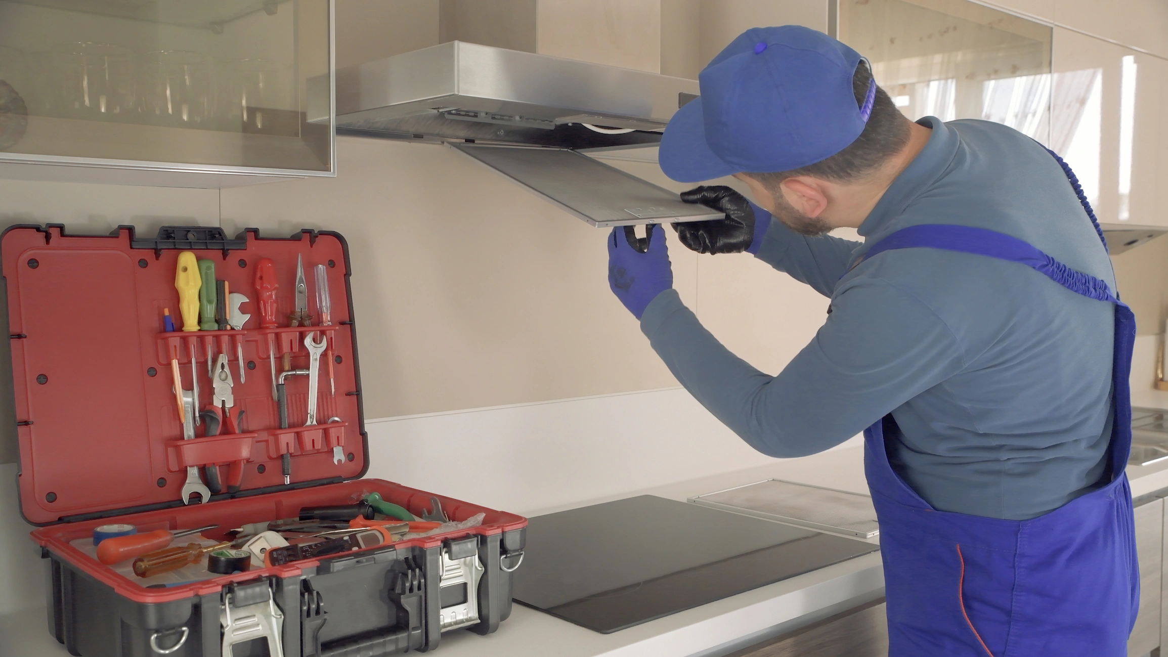 A man in overalls repairs a stove, emphasizing the importance of safety in kitchen environments with professional vent hoods.