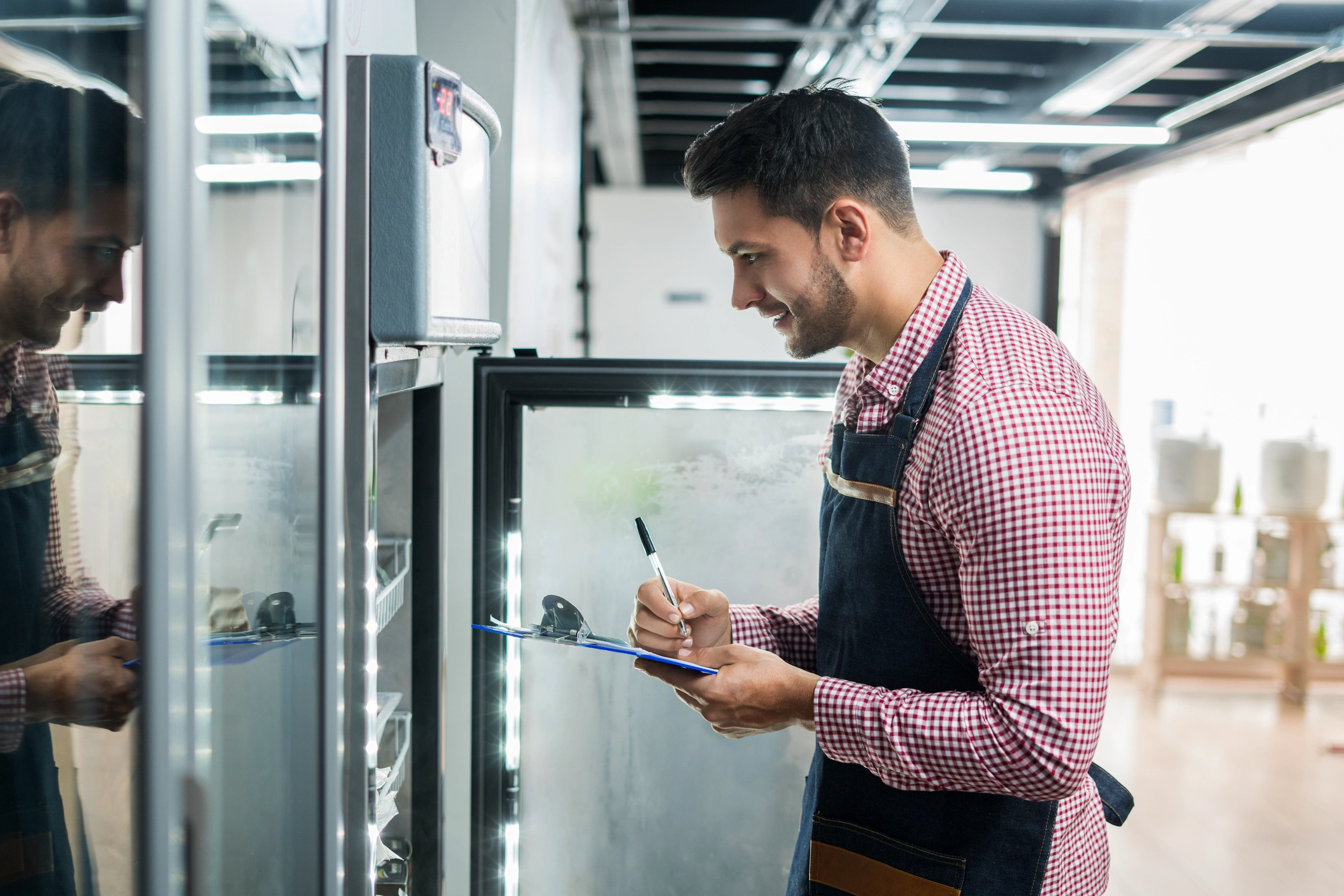 A man writes on a clipboard inside a walk-in freezer, surrounded by shelves of frozen goods.