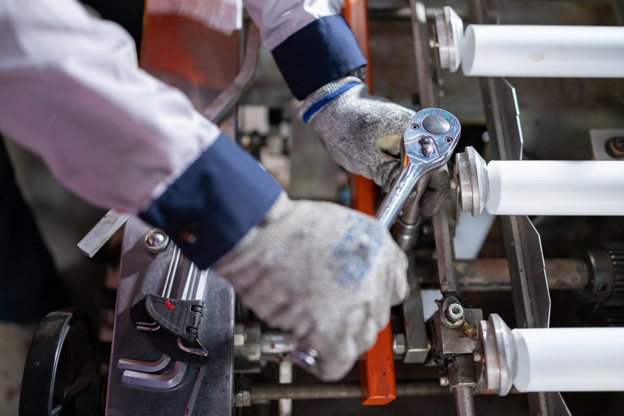 Worker wearing gloves uses a wrench on machinery in a factory.