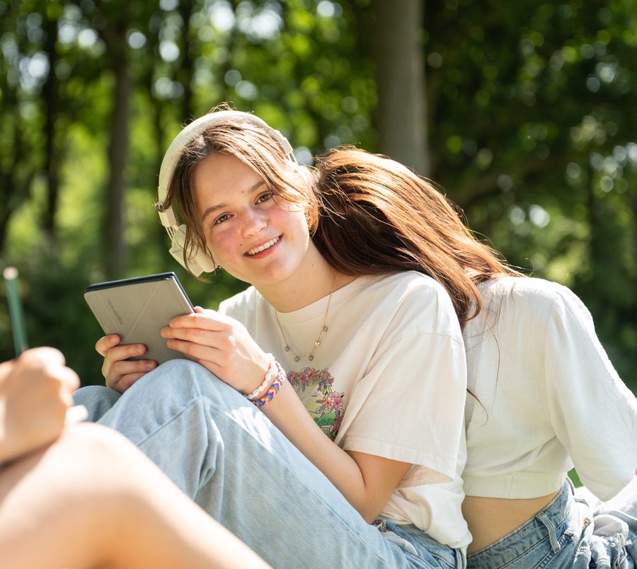 Leerling met koptelefoon en e-reader in het gras