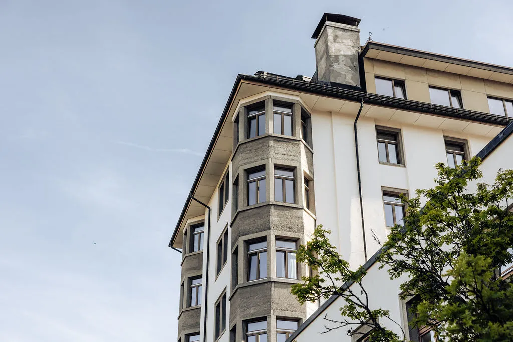 Corner of a multi-story building with gray stone and white walls under a clear sky.