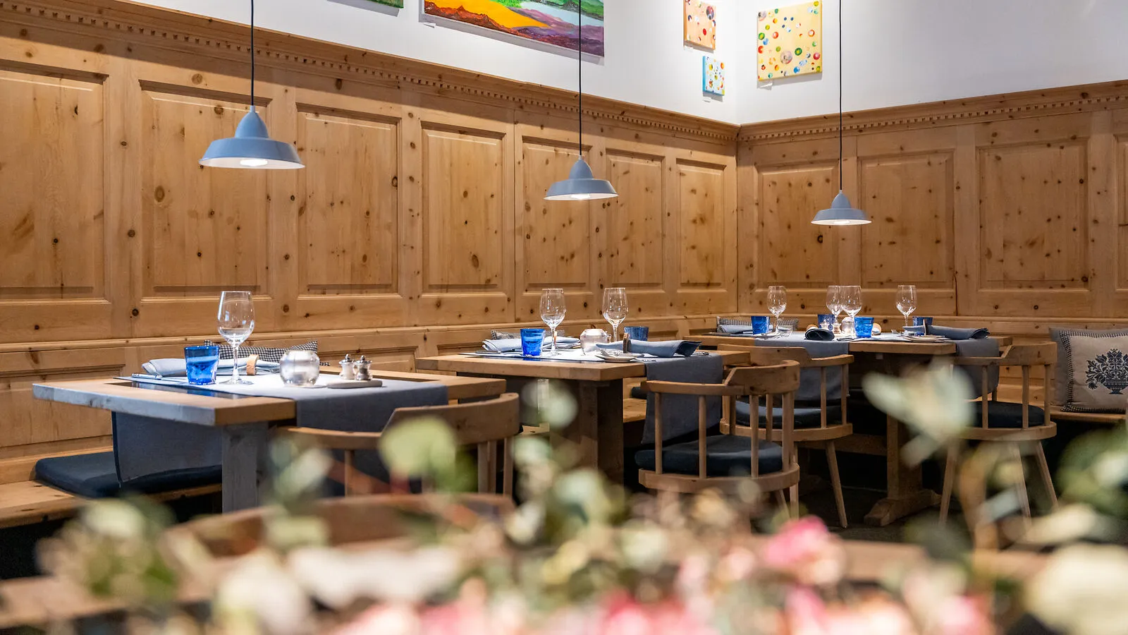Cozy restaurant interior with wooden paneling, tables set with blue glasses and hanging pendant lights.