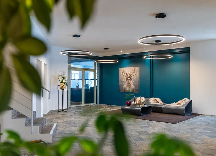 Modern lobby with stone flooring, circular pendant lights, teal accent wall, and seating area with fur throws.