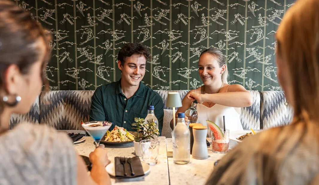 Two people at a table smiling while others watch as a woman opens a water bottle in a restaurant.