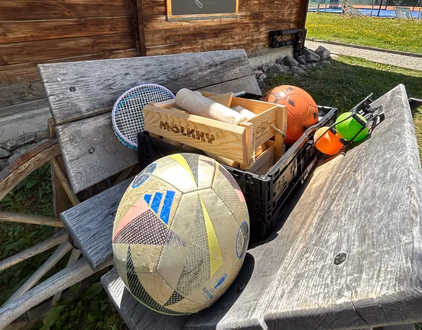 Outdoor games equipment on a wooden bench at Altein, Arosa, with a football, Moelkky set and badminton racket