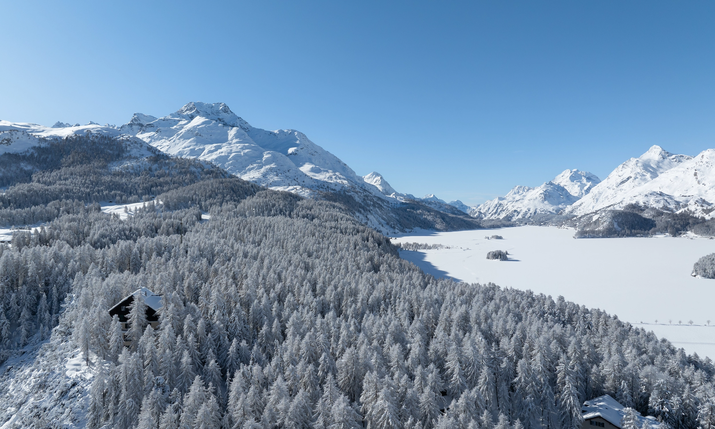 Lush green mountain valley with a small blue lake and winding trails, under partly cloudy skies.