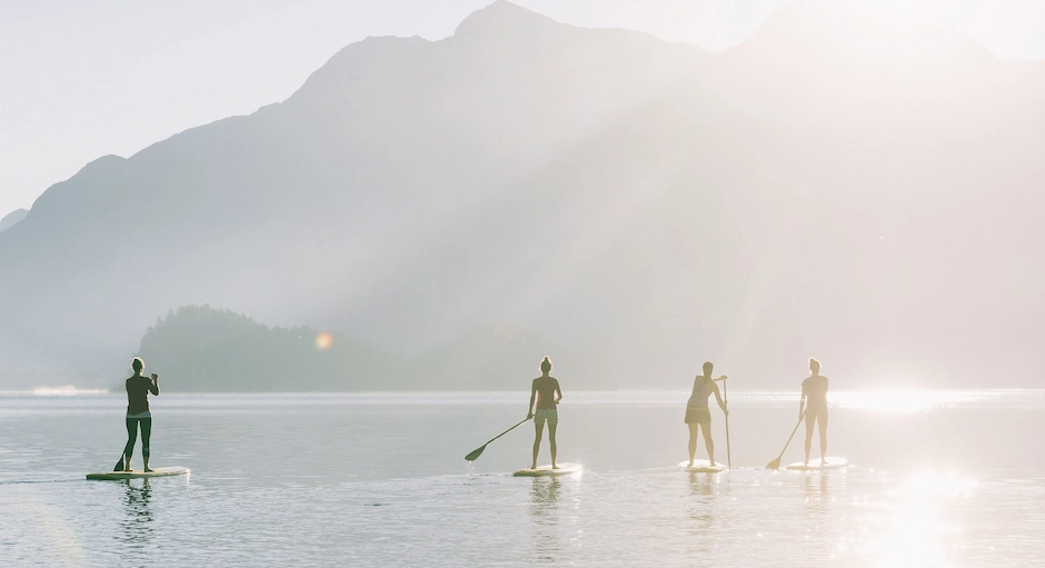 Four people paddleboarding on a misty lake at sunrise with mountains in the background.