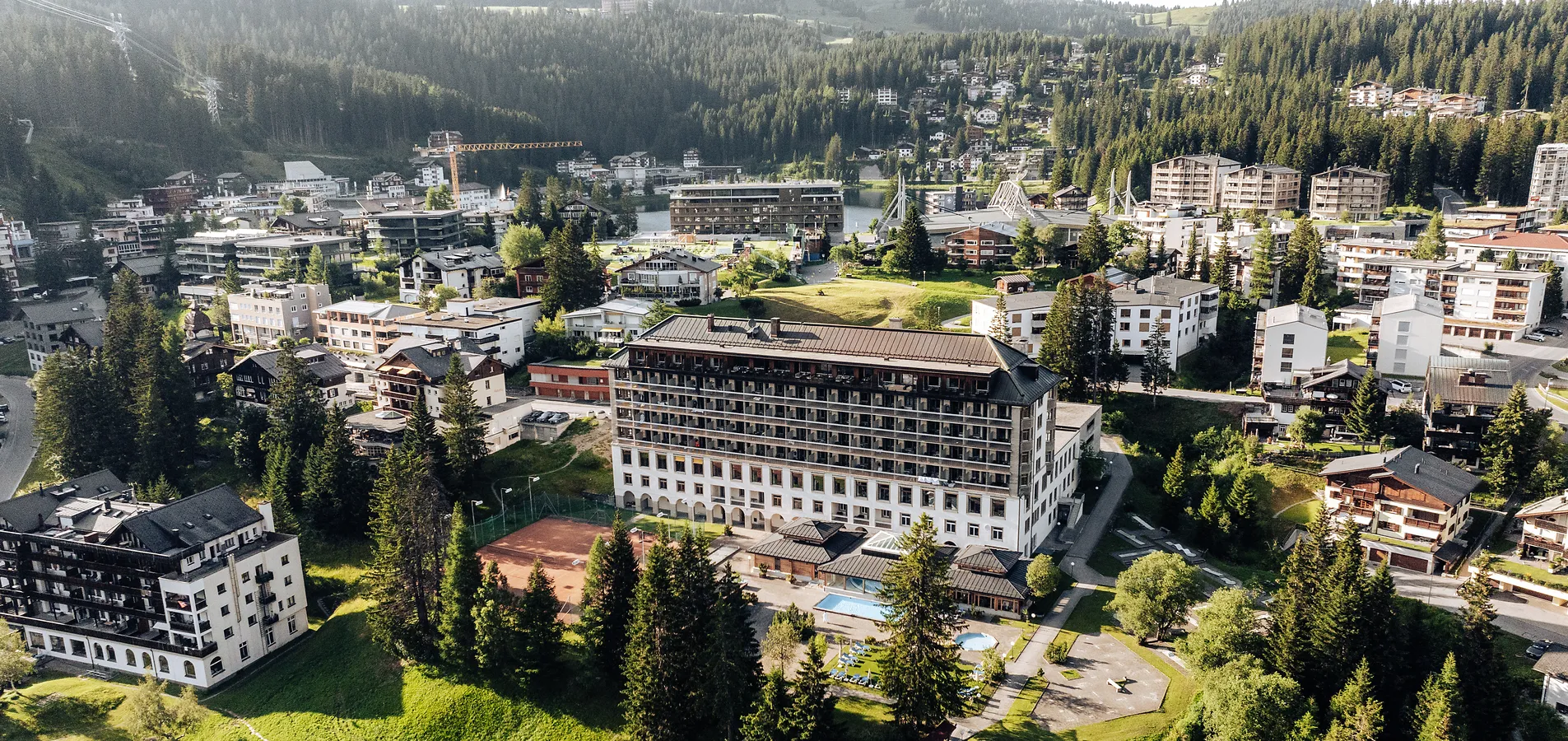 Lush green mountain valley with a small blue lake and winding trails, under partly cloudy skies.