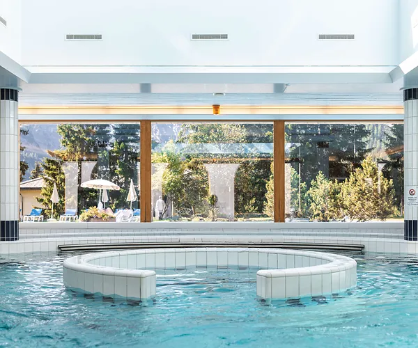 Indoor pool with circular built-in seating area and large windows showing trees and mountains outside.