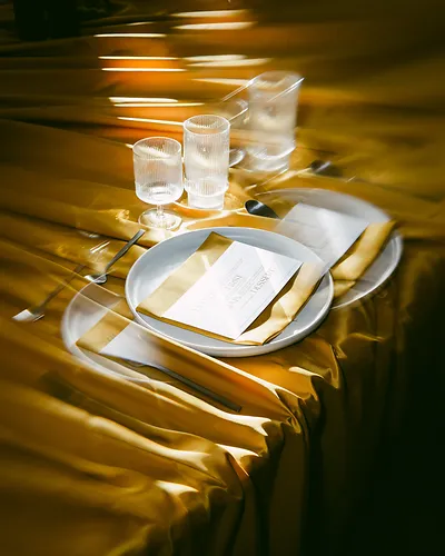 Elegant table setting with gold satin tablecloth, white plates, menu card, and glassware.