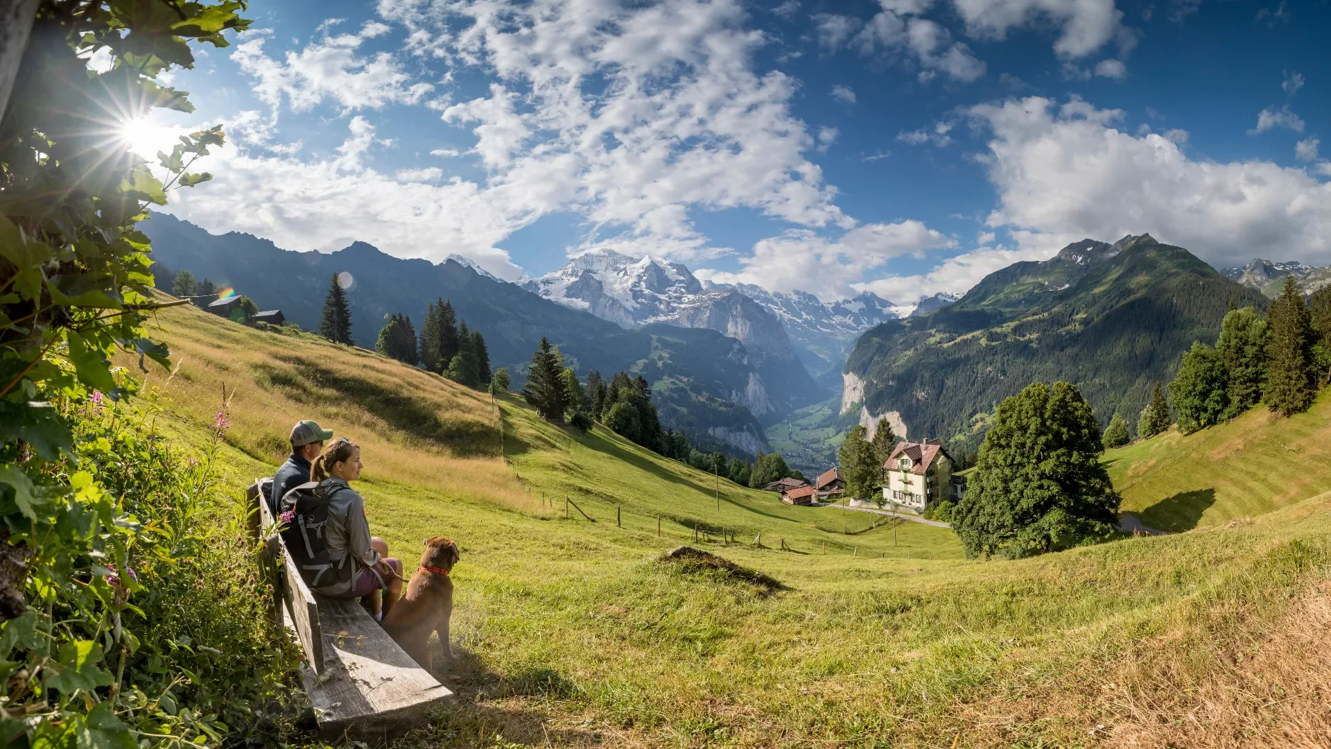 Couple resting on a wooden bench above Wengen with the Lauterbrunnen valley and snow-capped peaks behind.