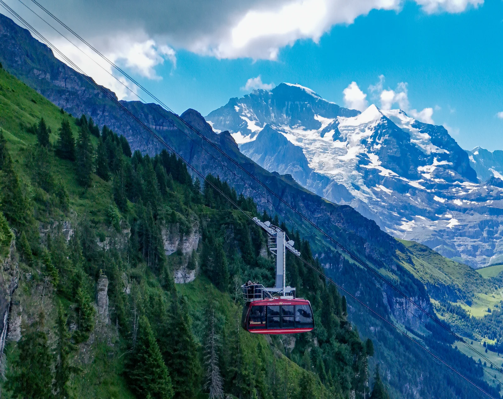 Cable car gliding above Wengen towards Männlichen with snow-capped peaks behind