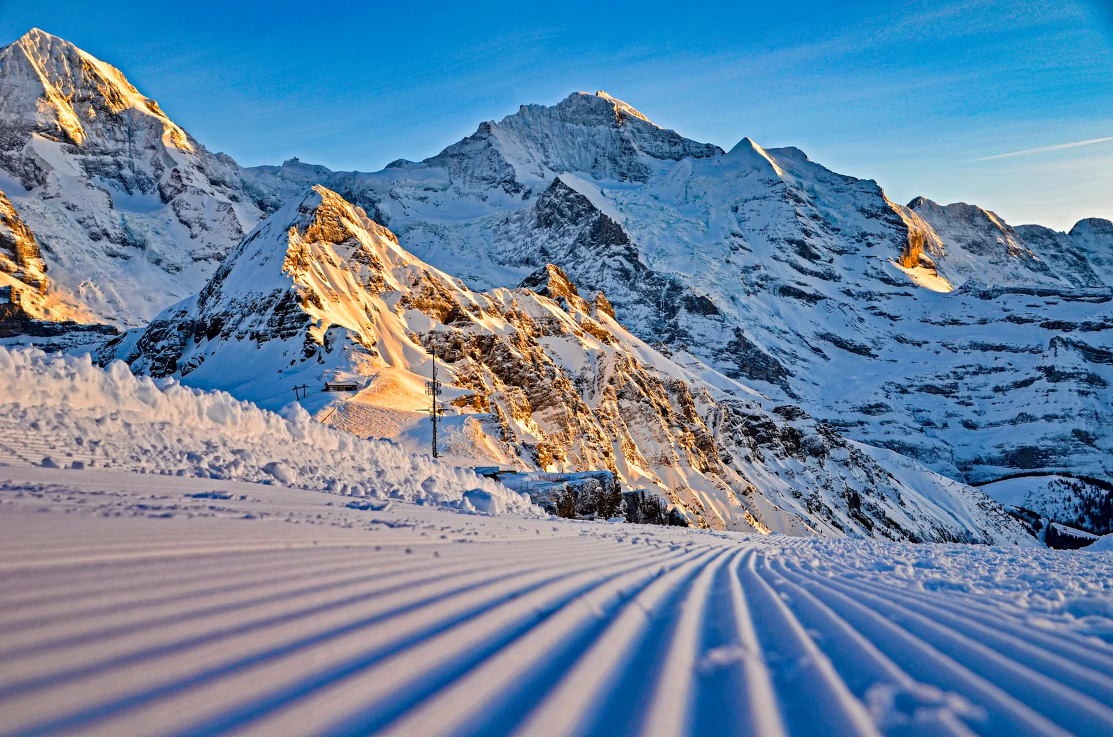 Eine frisch präparierte Skipiste im Morgengrauen über Wengen vor Eiger und Mönch