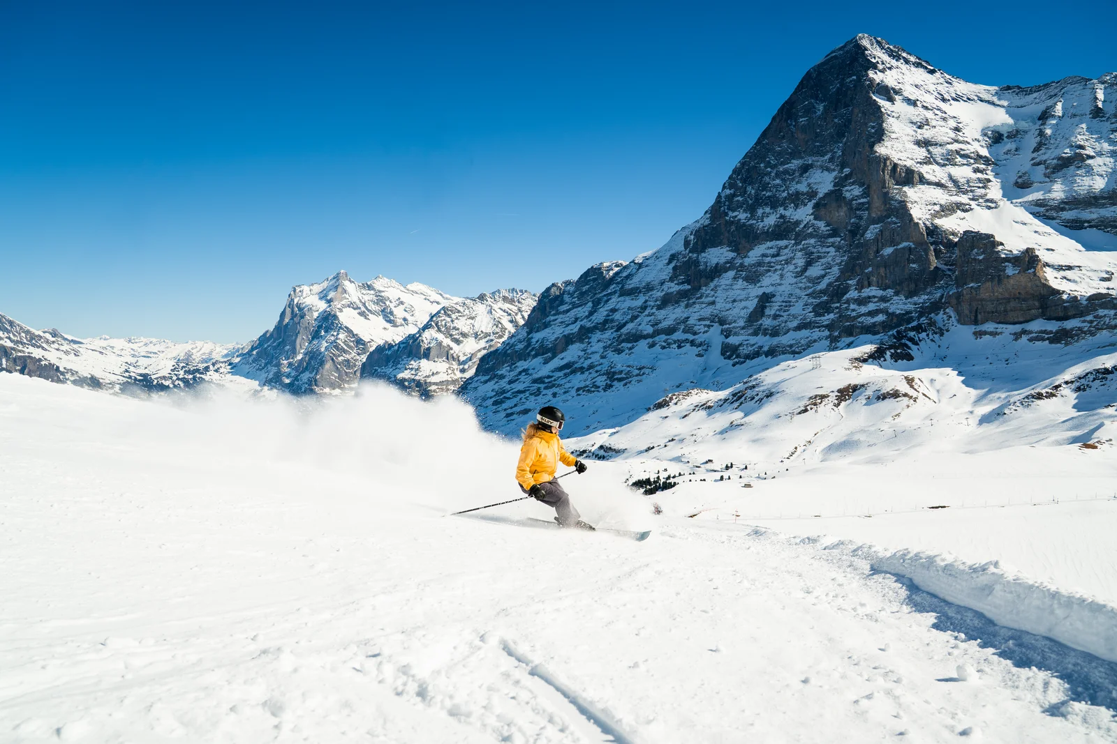 Eine Skifahrerin zieht einen Schwung auf einer Piste über Wengen, im Hintergrund Eiger, Mönch und Jungfrau