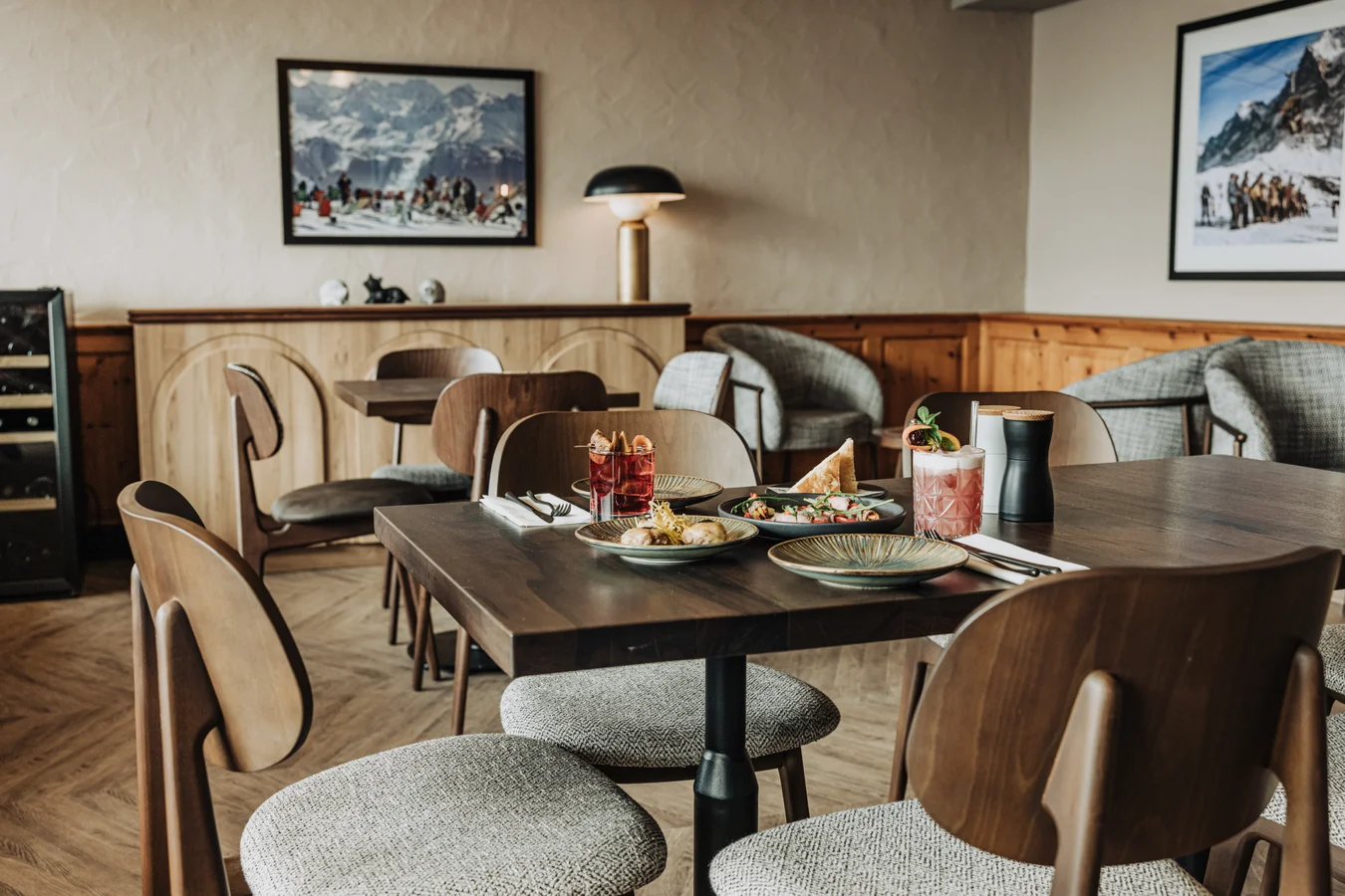 Intérieur du restaurant Alpensand à l’Altein, Arosa, avec des tables en bois sombre dressées de petites assiettes, des chaises en bois courbé et des tableaux de montagne encadrés