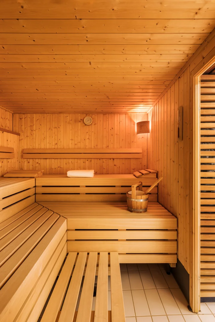La cabine de sauna en bois de l’hôtel Altein à Arosa, avec ses bancs étagés, un seau et une louche en bois et une serviette pliée